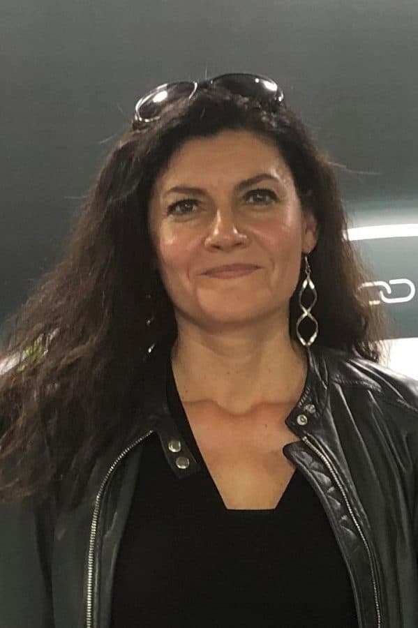 A woman with short hair smiles confidently, wearing a black blazer, in a professional setting.