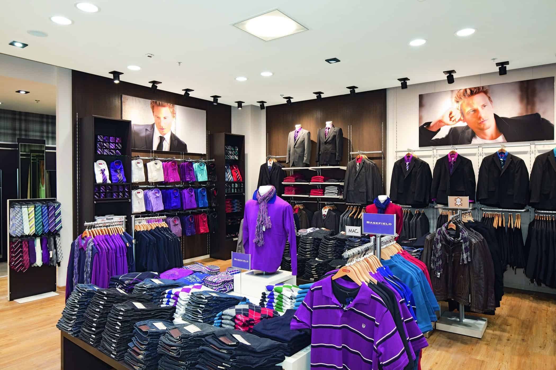 A department store men's section with various clothing displays and shoppers browsing through the merchandise.